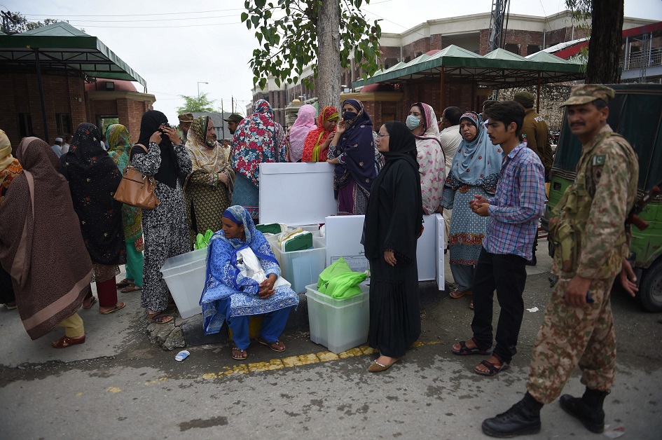An army soldier and presiding officers wait for transport after getting voting materials at a distribution centre in Rawalpindi. PHOTO: AFP