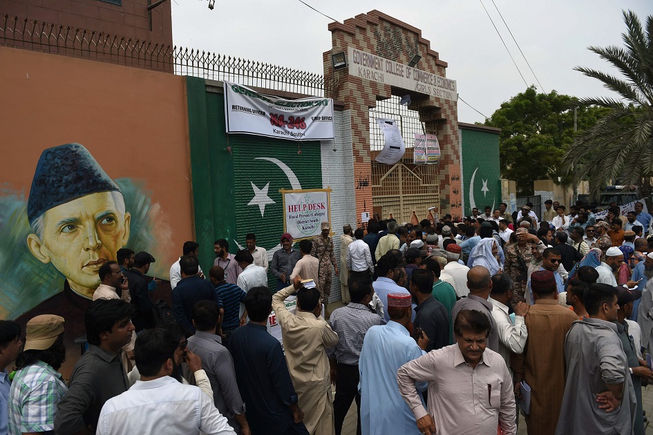 Pakistani election officials wait outside a distribution center to collect ballot boxes and voting materials in Karachi. PHOTO: AFP