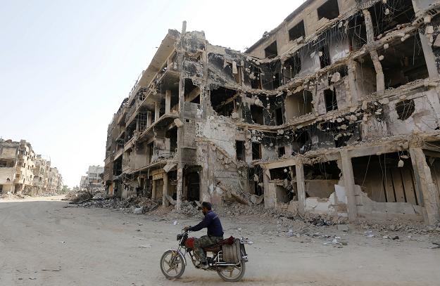 A man rides a motorbike by destroyed buildings in Harasta, on the outskirt of the Syrian capital Damascus. PHOTO: AFP.