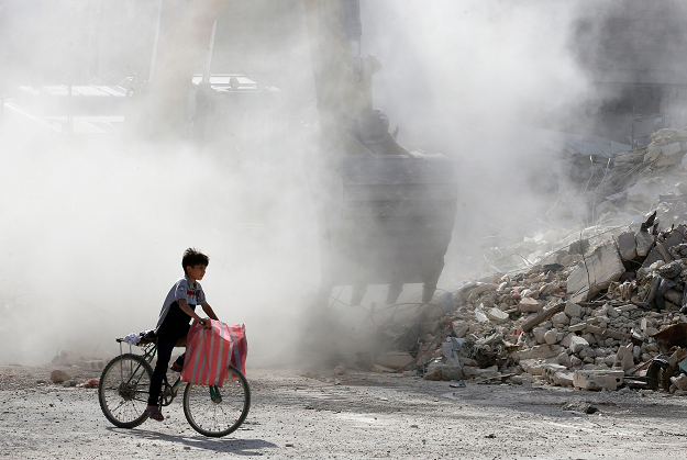 A Syrian boy rides his bicycle amid the rubble of destroyed buildings being removed by a bulldozer. PHOTO: AFP.