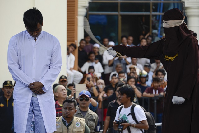 A member of Indonesia's police (R) whips a man (L) accused of having gay sex during a public caning ceremony outside a mosque in Banda Aceh, capital of Aceh province on July 13, 2018