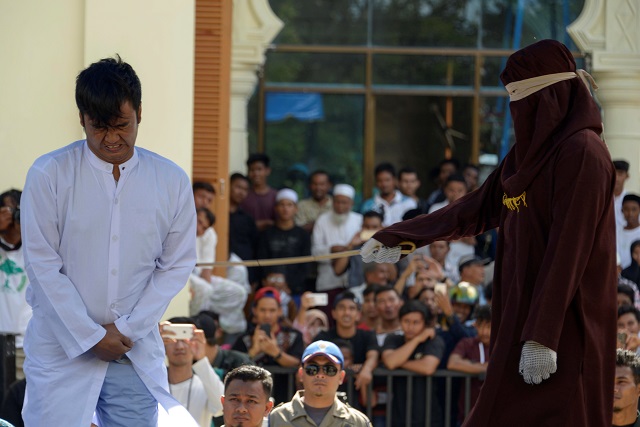 A member of Indonesia's police (R) whips a man (L) accused of having gay sex during a public caning ceremony outside a mosque in Banda Aceh, capital of Aceh province on July 13, 2018. PHOTO: AFP