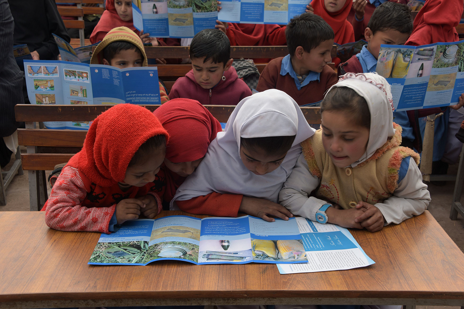 Students looking at pamphlets for an awareness campaign about landmines, provided by the Pakistan Red Crescent Society (PRCS), in Abbaspur Sector. PHOTO: AFP. 