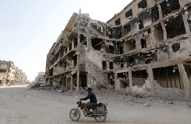 a man rides a motorbike by destroyed buildings in harasta on the outskirt of the syrian capital damascus photo afp