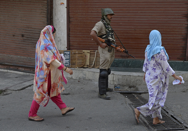 An Indian paramilitary trooper stands guard as Kashmiri women walk past during the first day of a strike. PHOTO:AFP