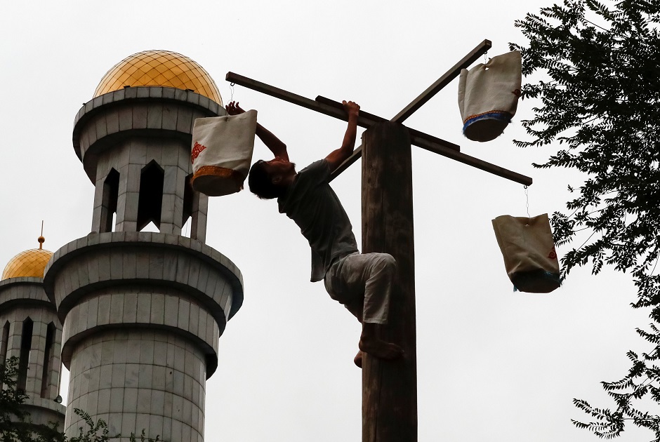 A man climbs on a pole to get a prize as he attends a competition to mark Eidul Azha, at the Central Mosque in Almaty, Kazakhstan on August 21, 2018. PHOTO:REUTERS
