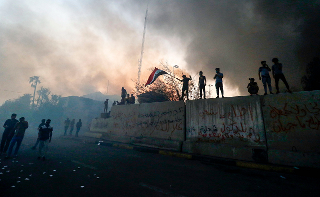 iraqi protesters wave a national flag while demonstrating outside the burnt down local government headquarter photo afp