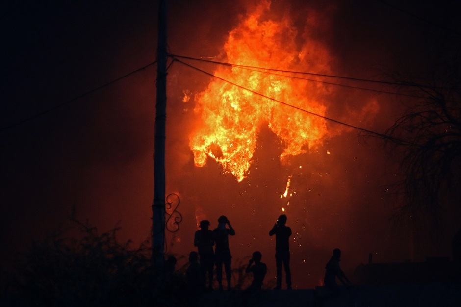 6.Iraqi protesters watch on official building in flames as they demonstrate against the government and the lack of basic services in Basra on September 6, 2018. - A curfew was imposed in the southern Iraqi city of Basra on September 6 as a fresh outbreak of violent protests left one person dead and 35 injured, officials said. PHOTO: AFP