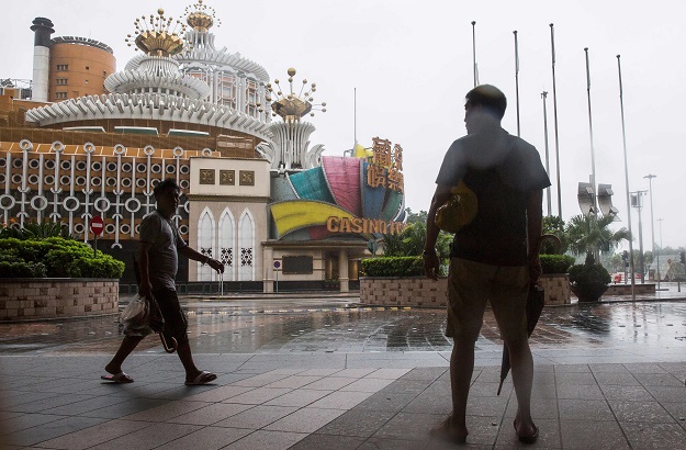 A pedestrian (L) walks past the Grand Lisboa which has closed its casino as super Typhoon Mangkhut edges closer to Macau on September 16, 2018. - Super Typhoon Mangkhut has smashed through the Philippines, as the biggest storm to hit the region this year claimed the lives of its first victims and forced tens of thousands to flee their homes. PHOTO: AFP