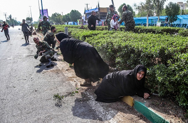 This picture taken on September 22, 2018 in the southwestern Iranian city of Ahvaz shows Iranian women and soldiers taking cover next to bushes at the scene of an attack. PHOTO: AFP