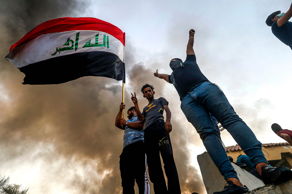 Iraqi protesters wave a national flag while demonstrating outside the burnt-down local government headquarters in Basra AFP