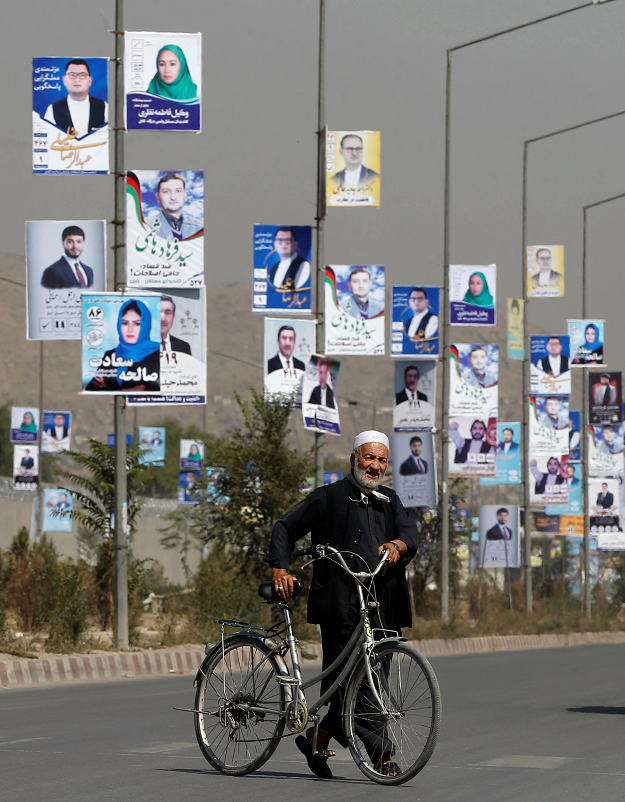  A man walks with his bicycle in front of election posters of parliamentary candidates during the first day of election campaign in Kabul. PHOTO: REUTERS