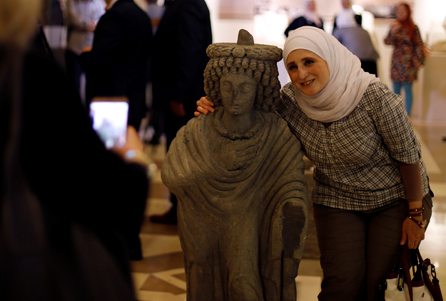 A woman poses for a picture with a restored sculpture, displayed in an exhibition, at the Opera house in Damascus, Syria  REUTERS