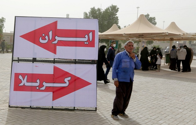 A man stands next to a sign that reads in Farsi and Arabic 