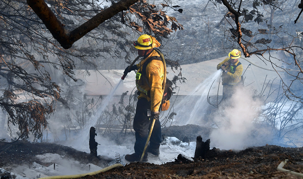 Firefighters spray foam on hot embers along a hillside near homes on Latigo Canyon Road. PHOTO: AFP