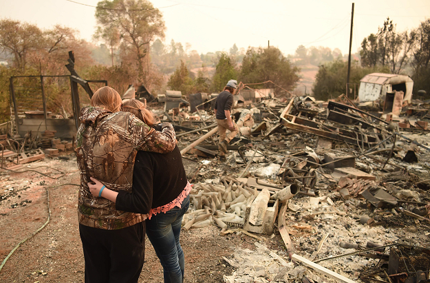 Kimberly Spainhower hugs her daughter Chloe, 13, while her husband Ryan Spainhower (R) searches through the ashes of their burned home in Paradise. PHOTO: AFP