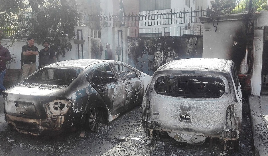 Pakistani security personnel stand next to burned out vehicles in front of the Chinese consulate. PHOTO: AFP