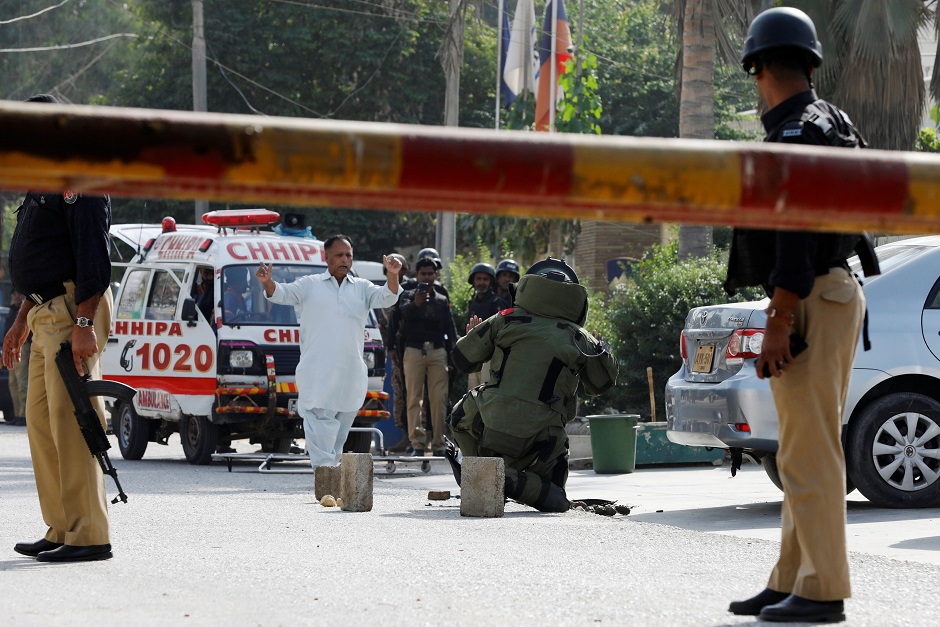 Police officers stand guard as a member of the bomb disposal unit (C) checks a bag with exlosives (unseen), after an attack on the Chinese embassy. PHOTO: REUTERS