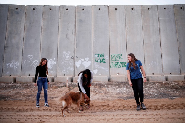  Israeli teens, Meshy Elmkies (R), 16, Liam Yefet (C), 16 and Lee Cohen, 17, co-managers of Instagram account, Otef.Gaza, play with a dog near a barrier which borders the Gaza Strip, in Kibbutz Kerem Shalom in southern Israel. PHOTO: REUTERS