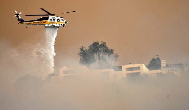  A Los Angeles County Fire Department firehawk makes a water drop through the thick smoke on homes in the hills of Malibu, as the Woosley Fire approaches PHOTO: REUTERS