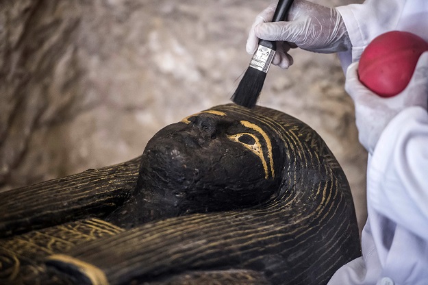 2.An Egyptian archaeologist brushes the top of a carved black wooden sarcophagus inlaid with gilded sheets, dating to Egypt's Late period (7th-4th century BC) discovered by an Egyptian archaelogical mission at Al-Assasif necropolis on the west bank of the Nile north of the southern Egyptian city of Luxor PHOTO: AFP