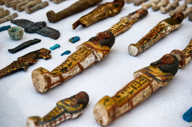 This picture shows carved wooden statues and funerary figurines called 'Ushabtis' made of wood, faience and clay laid out on a table, discovered by an Egyptian archaelogical mission at tomb TT28 PHOTO: AFP 