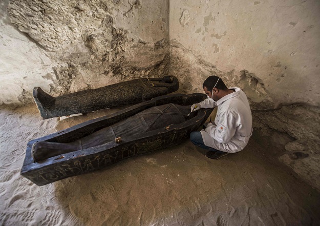 5.An Egyptian archaeologist brushes a mummy laid inside a carved black wooden sarcophagus inlaid with gilded sheets, dating to Egypt's Late period (7th-4th century BC) PHOTO: AFP