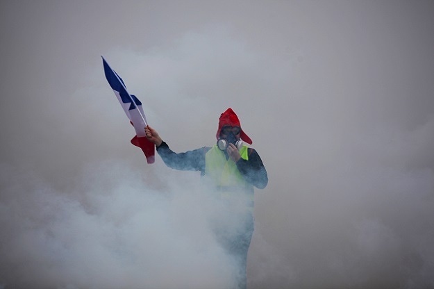 A demonstrator holds a French flag as he walks amid the tear gas during a protest of Yellow vests (Gilets jaunes) against rising oil prices and living costs, on December 1, 2018 in Paris. PHOTO:AFP