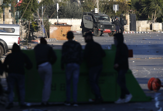 Palestinian youth stand facing Israeli troops after a house belonging to a Palestinian accused of killing an Israeli soldier a few months ago was blown up in Ramallah in the Israeli-occupied West Bank on December 15, 2018. PHOTO: AFP