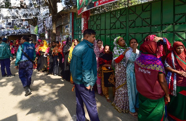 Bangladeshi voters wait in line outside a polling station while security police officials watch over in Dhaka. PHOTO: AFP