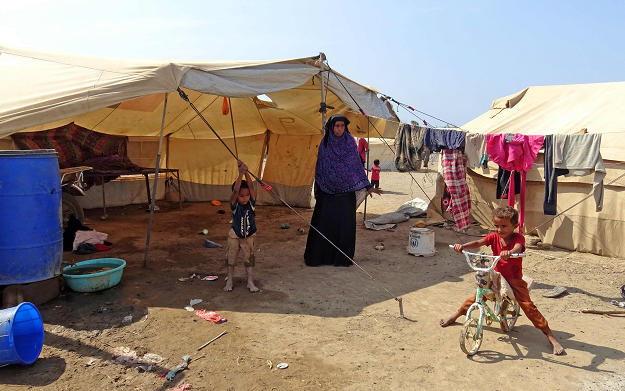 A Yemeni woman stands in front of a tent as children play at a camp for displaced people in the Khokha district of the western province of Hodeidah on December 11, 2018. PHOTO: AFP