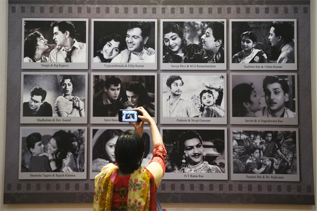 In this picture taken on January 22, 2019, a visitor takes a picture of a display with images of former Indian movie actors at the National Museum of Indian Cinema (NMIC), the country's first museum showcasing the history of its film industry, in Mumbai. - From silent black-and-white films to colourful blockbusters bursting with song and dance, a new museum tracing the evolution of Indian cinema has opened in the home of Bollywood. Costing 1.4 billion rupees (19.6 million USD), India's first national film museum is spread across a stylish 19th-century bungalow and a modern five-storey glass structure in south Mumbai. (Photo by PUNIT PARANJPE / AFP) 