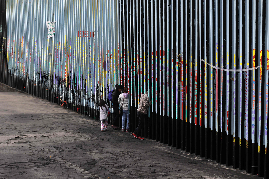 A family of Central American migrants look through the US-Mexico border fence, as seen from Playas de Tijuana, in Baja California state, Mexico, on January 16, 2019. - Hundreds of Hondurans have set out on a trek to the United States, forming another caravan, which US President Donald Trump cited Tuesday to justify building a wall on the border with Mexico. PHOTO: AFP