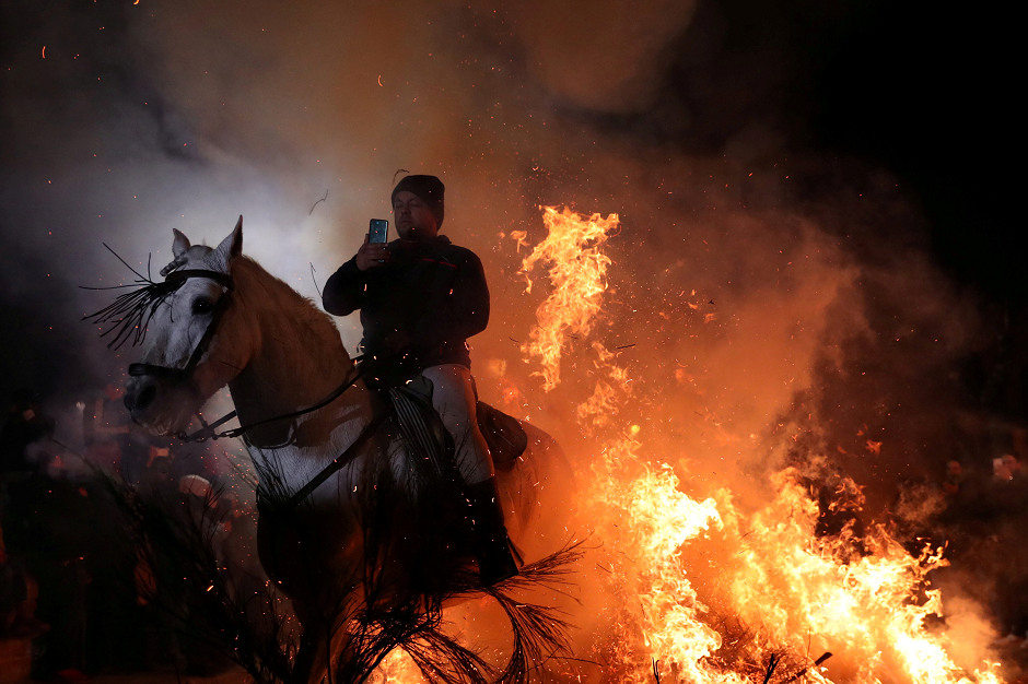 A man points a phone to himself riding a horse through flames during the annual 