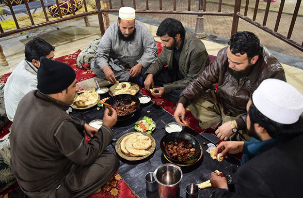 In this picture taken on December 6, 2018, Pakistani customers eat grilled meat at the Charsi (Hashish) Tikka restaurant in Namak Mandi in Peshawar. - The sweet aroma of mutton smoke drifts through a maze of crumbling alleyways, a barbecue tang that for decades has lured meat-eaters from across Pakistan to the frontier city of Peshawar. The ancient city, capital of northwestern Khyber Pakhtunkhwa province, has retained its reputation for some of Pakistan's tastiest cuisine despite taking the brunt of the country's bloody war with militancy. (Photo by ABDUL MAJEED / AFP) / To go with Pakistan-culture-food-bbq-Peshawar,FEATURE by David STOUT