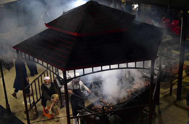 In this picture taken on December 6, 2018, a Pakistani man cooks grilled meat on a barbeque at the Charsi (Hashish) Tikka restaurant in Namak Mandi in Peshawar. - The sweet aroma of mutton smoke drifts through a maze of crumbling alleyways, a barbecue tang that for decades has lured meat-eaters from across Pakistan to the frontier city of Peshawar. The ancient city, capital of northwestern Khyber Pakhtunkhwa province, has retained its reputation for some of Pakistan's tastiest cuisine despite taking the brunt of the country's bloody war with militancy. (Photo by ABDUL MAJEED / AFP)