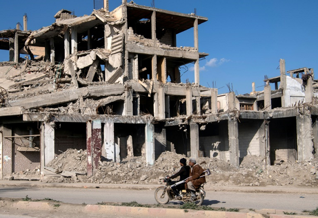 Syrian men ride a motorcycle past a destroyed building in the Islamic State group's former Syrian capital of Raqa in northern Syria. PHOTO: AFP