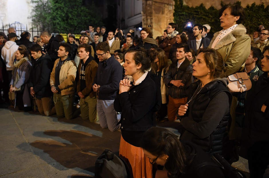 People kneel on the pavement as they pray outside watching flames engulf Notre-Dame Cathedral in Paris. PHOTO: AFP