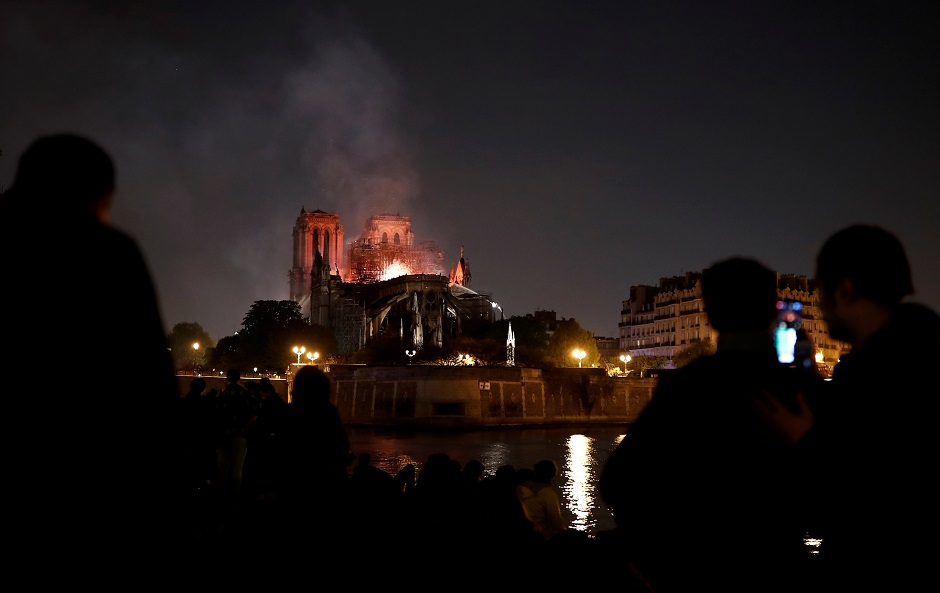 Bystanders look on as flames and smoke billow from the roof at Notre-Dame Cathedral in Paris. PHOTO: AFP