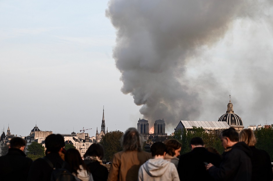 Bystanders look on as flames and smoke billow from the roof at Notre-Dame Cathedral in Paris. PHOTO: AFP