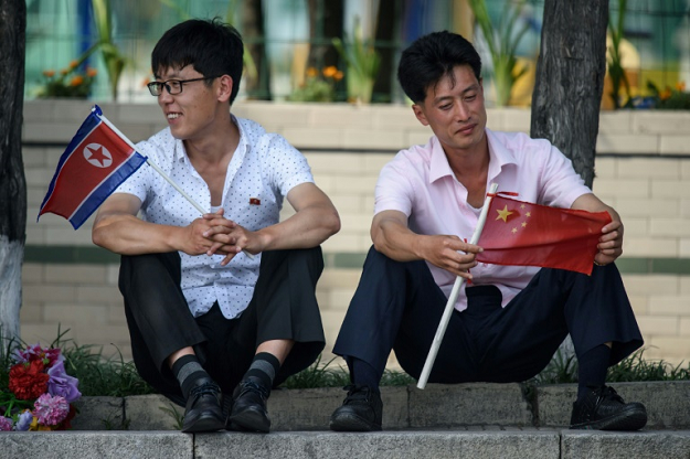Two men sit holding North Korean and Chinese flags near Kim Il Sung square in Pyongyang on June 20, 2019. PHOTO: AFP