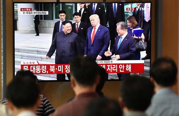 People watch a television news screen showing live footage of US President Donald Trump, South Korean Moon Jae-in and North Korean leader Kim Jong Un meeting at the truce village of Panmunjom in the DMZ, at a railway station in Seoul on June 30, 2019. PHOTO: AFP