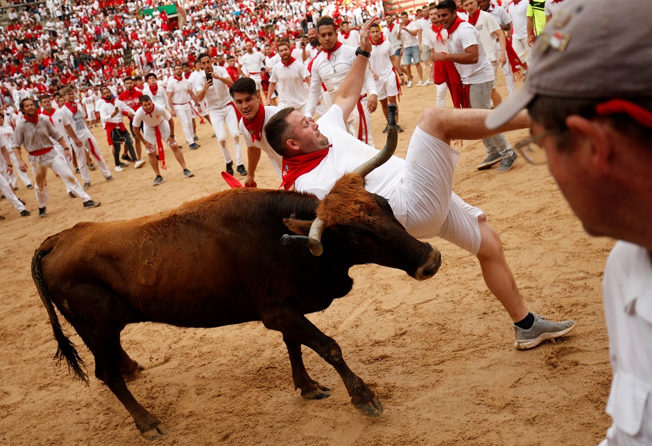 A reveller loses his balance near a wild cow in the bull ring after the running of the bulls. PHOTO: AFP.