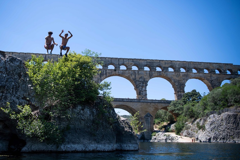 Two young men dive into the Gard river next to the Pont du Gard bridge on July 10, 2019 in Vers-Pont-du-Gard, southern France. PHOTO: Reuters.