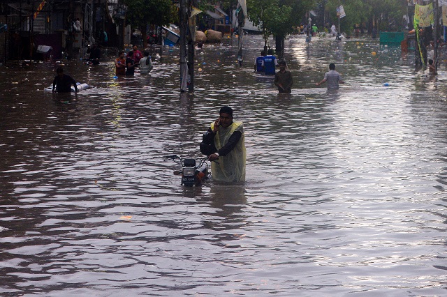 a pakistani man speaks on his phone while pushing his bike along a flooded street after heavy monsoon rains in lahore photo afp