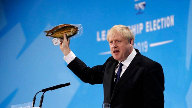 conservative mp and leadership contender boris johnson holds up kipper fish in plastic packaging as he speaks at the final conservative party leadership election hustings in london on july 17 2019 photo afp
