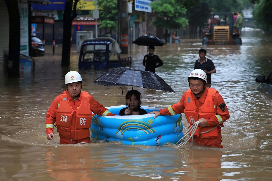 Rescue workers wade through flood waters as they evacuate a woman with an inflatable swimming pool on a street following heavy rainfall in Pingxiang:AFP