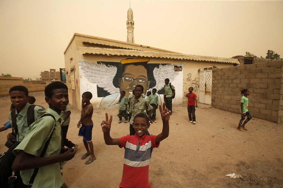 Pupils gesture in front of a mural painting of a protester killed during anti-government protests in the Sudanese capital Khartoum. PHOTO: AFP