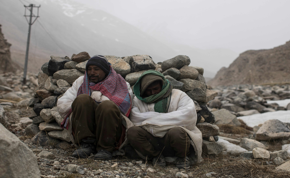 Raj Shekhar (L), 33, and Tej Narayan, 30, road maintenance workers from India's low-lying eastern Jharkhand state, take shelter behind rocks during inclement weather while working along Pangong Lake road near the Chang La pass in northern India's Ladakh region. Photo: AFP