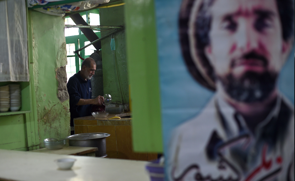 A cook washes dishes near a poster of Ahmad Shah Massoud, at a restaurant in Charikar in Parwan Province. Photo: AFP